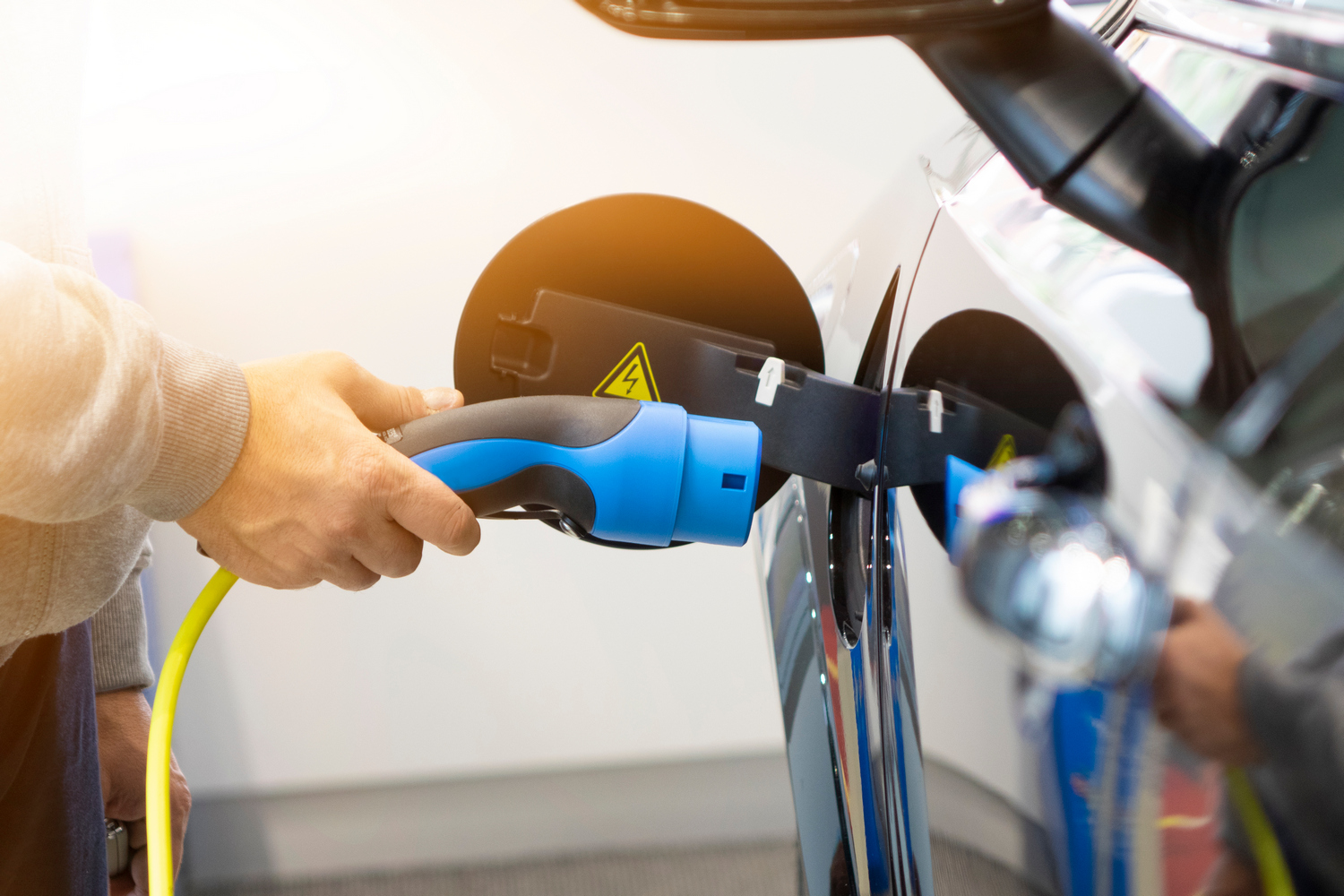 Man turning on charging of car. EV Car or Electric car at charging station with the power cable supply plugged in on blurred nature with soft light background. Eco-friendly alternative energy concept